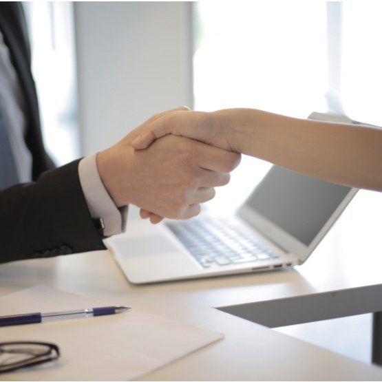 Two HR professionals shake hands over a white office desk.